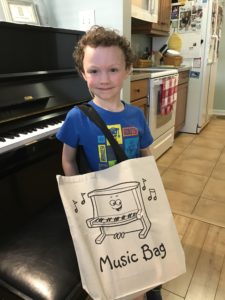 smiling young child standing at the piano with music bag